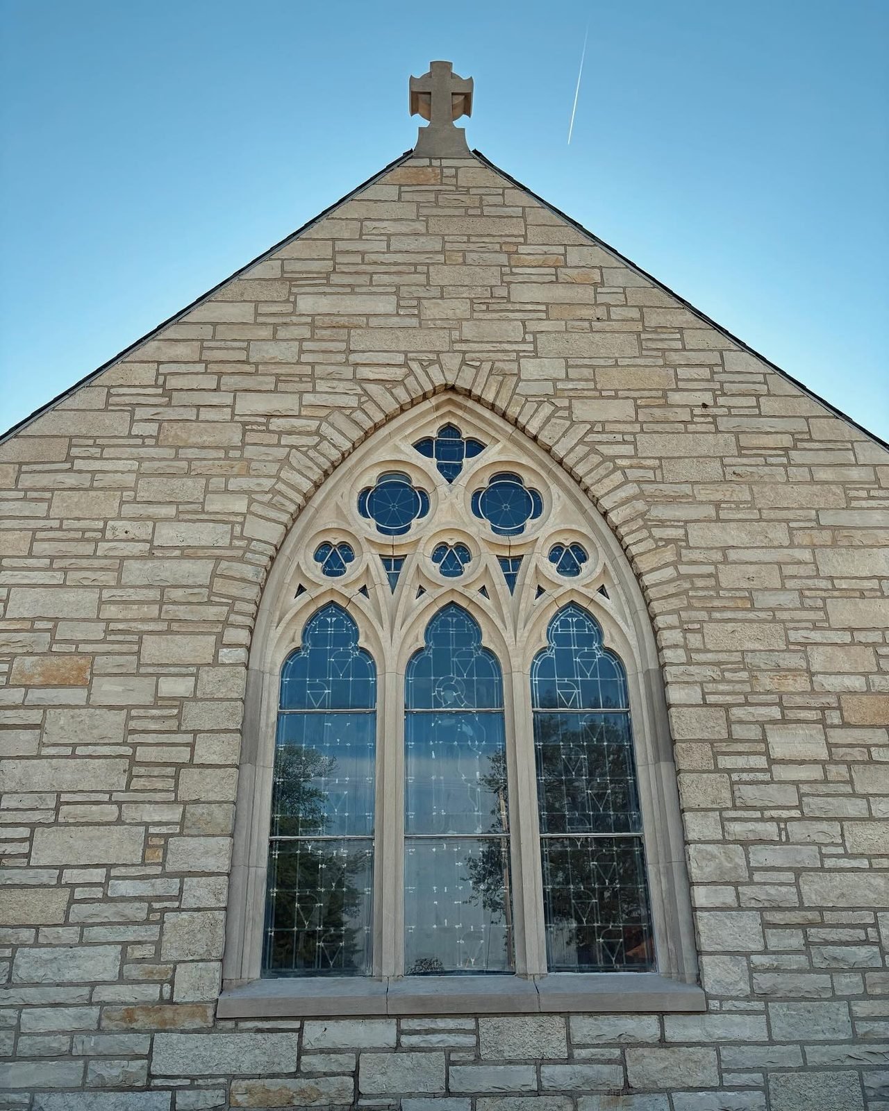 A tall Gothic stained-glass window in the restored stone church